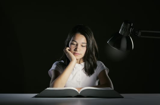 Young girl student, studying late into the night with her book and homework
