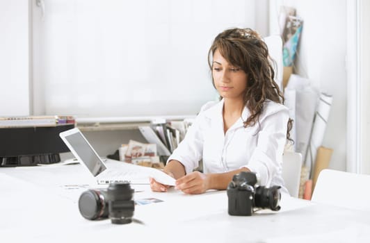 Female photographer examines the photographs, is sitting at her desk in the office