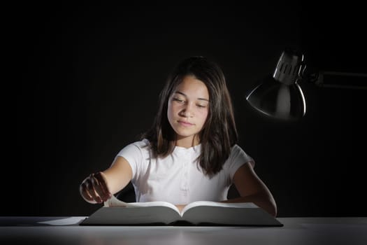 Young girl student, studying late into the night with her book and homework
