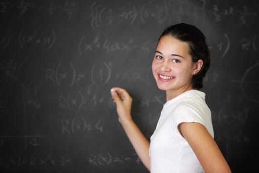 A young female student is standing in front of the blackboard going to draw something with a chalk.