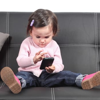 Cute baby browsing in a smartphone sitting on a black couch at home