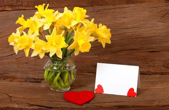 Blank white card with text space next to a bouquet of flowers on a rustic wooden surface