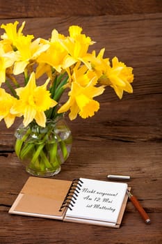 Notebook opened with the text "Don't forget! May 12 is Mother's Day"" and a pen lies on wooden ground"