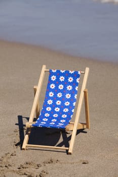 Wooden beach lounger with blue fabric pattern on the sandy beach