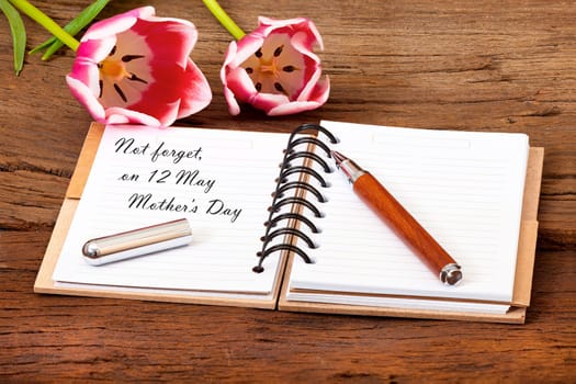 Mother ́s Day Event Reminder with a Flower,Notepad with Pen on old Wooden Background