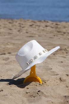 Straw hat hangs on yellow shovel on the beach