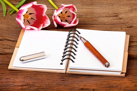 Notebook opened,a pen and two tulips lie on wooden ground