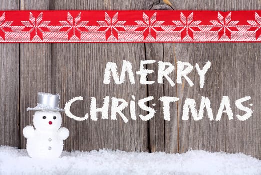 Christmas Greeting Card with a small Snowman and Snow Script on old wooden Board and a red-white Fabric Ribbon