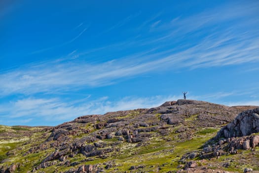 Man with a backpack on a mountain spread wide his hands in the summer against a blue sky with clouds