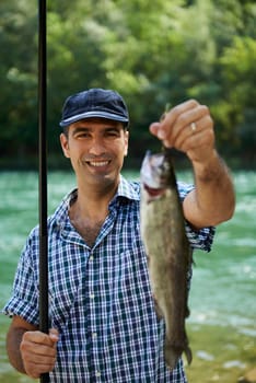 mid adult fisherman on holidays on river, relaxing and fishing trout. Focus on background