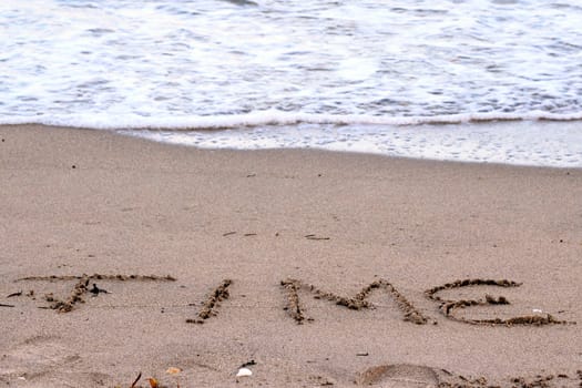 The word time carved in printed capital letters in sand on the beach a few feet away from the Atlantic coast water waves ready to be washed away during the daytime..