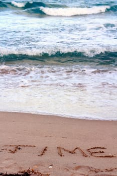 The word, time, written in the sand at the waters edge of the Atlantic ocean in the daytime.