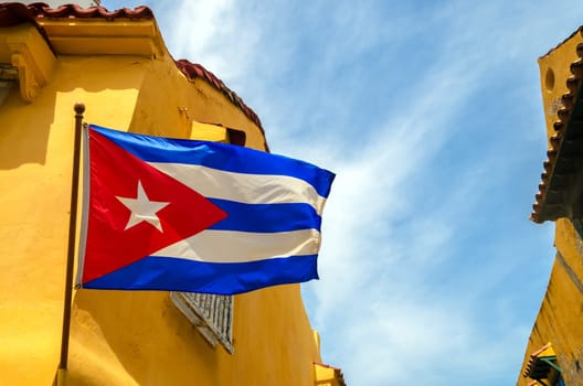 Cuban flag set against blue sky and yellow colonial buildings