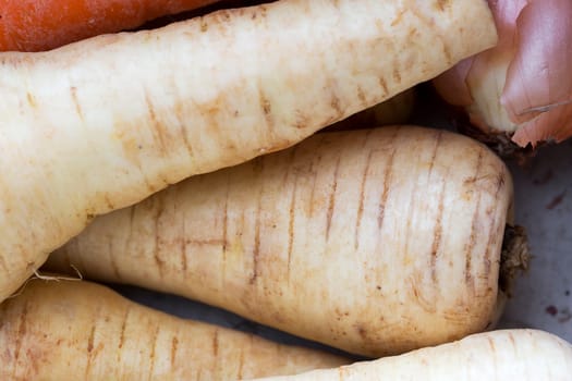 Close up of raw parsnips, with other vegetables barely visible.