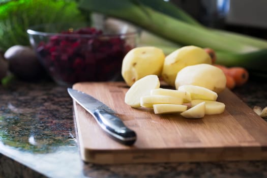 Peeled whole potatoes and sliced potatoes on cutting board with other ingredients in background