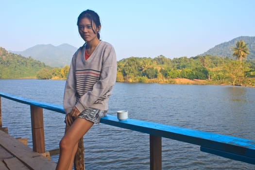 young girl and hot coffee in morning on river and mountain background