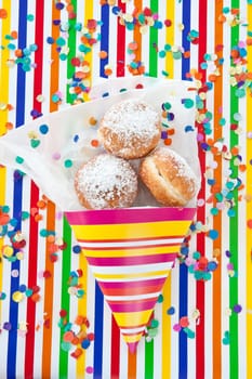 Fresh fritters in colorful bag on striped background