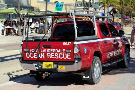 FORT LAUDERDALE, FLORIDA - FEBRUARY 5, 2013: Red ocean rescue truck seen parked on the sidewalk along State Road A1A on a sunny day with people dining at restaurants and walking in the background.