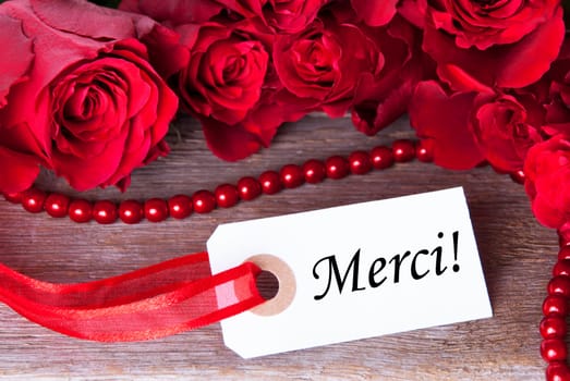 A Background with Red Roses and a White Ticket with the French Word Merci on it Which Means Thanks