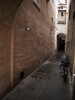 View of a narrow alley with a bike leaning against the wall and small lights on the left wall in Merano / South Tyrol