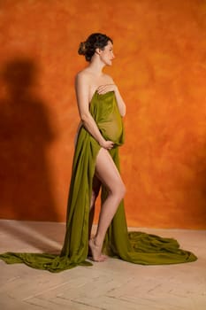 Pregnant Woman on an orange background covered with a green cloth
