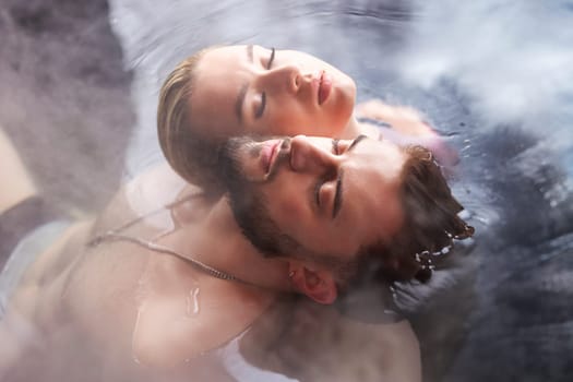 a young couple sits in a vat filled with water with their backs to each other