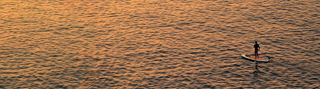 Adventurous people on a stand up paddle board is paddling during a bright and vibrant sunrise