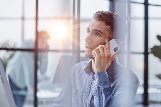 Portrait of young entrepreneur in casual office making phone call while working with laptop