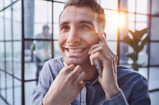 Portrait of young entrepreneur in casual office making phone call while working with laptop