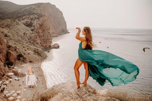 Woman sea green dress. Side view a happy woman with long hair in a long mint dress posing on a beach with calm sea bokeh lights on sunny day. Girl on the nature on blue sky background