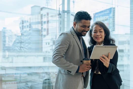 Two happy diverse coworker discussing report on tablet, working on project together.