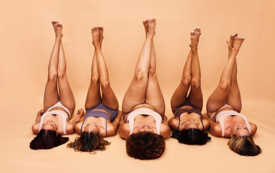Beauty, diversity and legs of women in studio for skincare, comparison or wellness on wall background. Difference, beauty and female friends relax in a line with feet up for glowing skin or treatment.