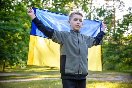 Pray for Ukraine. boy with Ukrainian flag running the summer park. Little kid waving national flag praying for peace. Happy child celebrating Independence Day.