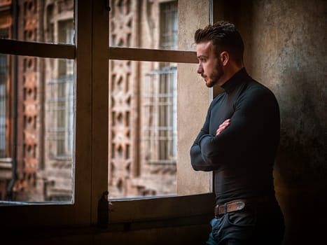 A man standing in front of a window with his arms crossed arms. Photo of a confident man with crossed arms standing in front of a window