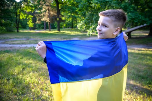 Pray for Ukraine. boy with Ukrainian flag running the summer park. Little kid waving national flag praying for peace. Happy child celebrating Independence Day.