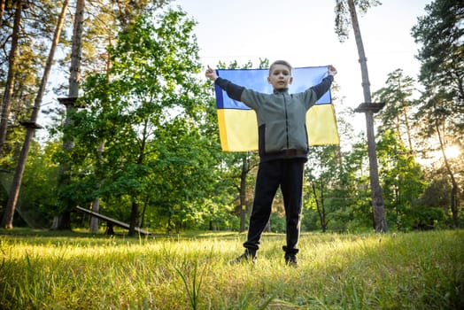 Pray for Ukraine. boy with Ukrainian flag running the summer park. Little kid waving national flag praying for peace. Happy child celebrating Independence Day.