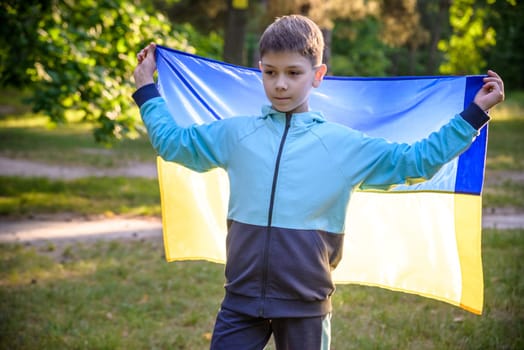 Pray for Ukraine. boy with Ukrainian flag running the summer park. Little kid waving national flag praying for peace. Happy child celebrating Independence Day.