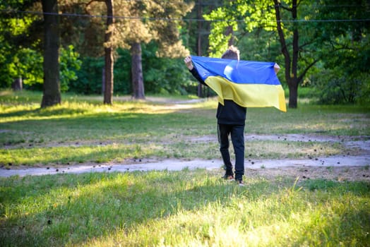 Pray for Ukraine. boy with Ukrainian flag running the summer park. Little kid waving national flag praying for peace. Happy child celebrating Independence Day.