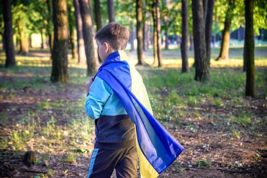 Worried teenager patriot wear blue yellow Ukrainian flag on his shoulders. Spring nature background. Ukraine national symbol. Patriotism.