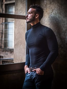 A man standing in front of a window. Photo of a confident man with hands in pockets standing in front of a window