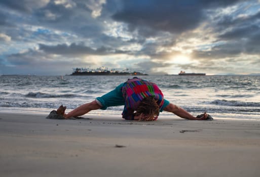 A person is bending over on the beach, doing yoga exercise or stretching