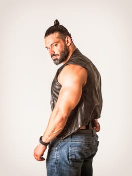 A man in a leather vest is looking at camera, hiding a gun in his jeans with a menacing look in his eyes