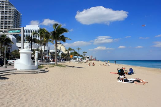 FORT LAUDERDALE, FLORIDA - MARCH 3, 2013: People relaxing at the Atlantic coast beach at the end of Bayshore Drive off modern and busy State Road A1A on a sunny and warm mostly blue sky winter day.