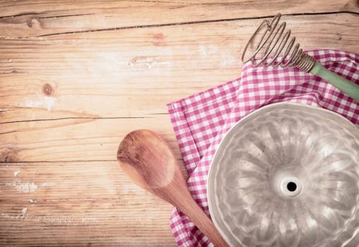 Old circular metal baking mould for cooking a ring cake or flan lying upside down on a fresh red and white checked cloth on a rustic wooden table, overhead view