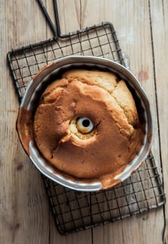 Freshly baked ring cake cooling on an old wire rack still in its circular mould, overhead view