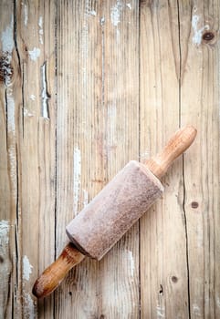 Old small wooden rolling pin covered in a thin layer of flour from baking and rolling dough lying on a wooden table in a country kitchen, overhead, view with copyspace