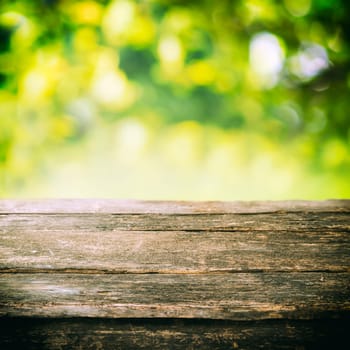 Empty rustic wooden board or old weathered garden table top with summer greenery and golden sunlight in the background