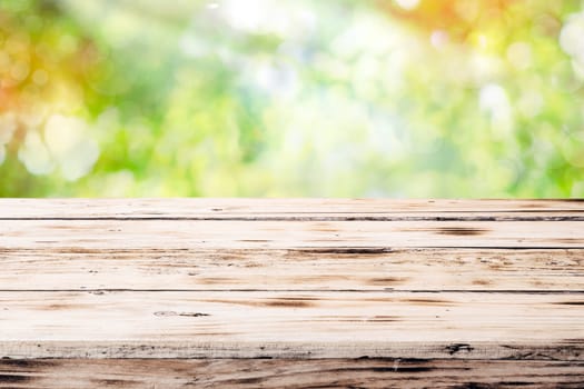 Old empty rustic grunge wooden table top against a blurred green blurred outdoor backgorund with copyspace
