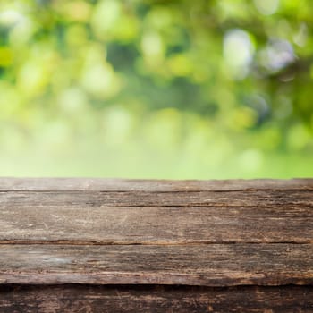 Rustic weathered cracked wooden country fence plank or table top against a blurred background of greenery and foliage in summer sun