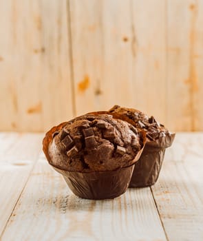 Two delicious fresh chocolate chip muffins in brown paper cups on a rustic wooden table in a country kitchen